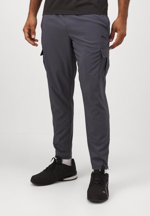 Pantalones cargo grises con bolsillos laterales, hechos de material ligero. Cuentan con una cintura elástica y un diseño de ajuste ceñido. Combinados con zapatillas deportivas negras.
