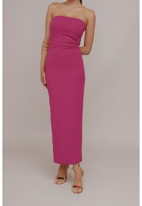 Abito longuette aderente e senza spalline in un vivace rosa, realizzato in un tessuto liscio. Presenta una vita arricciata e arriva fino alla caviglia. Accentato con tacchi dorati.