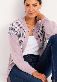 Ljusrosa stickad cardigan med en geometrisk mönstrad ok i grått och vitt. Har rund halsringning, knappstängning och ribbade ärmslut.