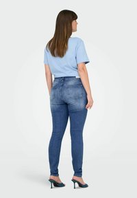 Camiseta de manga corta azul combinada con unos jeans ajustados de tiro alto en color oscuro. Los jeans tienen un lavado desgastado y dos bolsillos traseros.