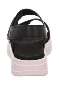 Černá sandála s širokými pásky, platformovou podrážkou a bílým gumovým spodkem. Pohled zezadu ukazuje texturovanou stélku a oporu paty.