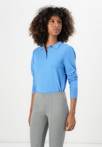 Lichtblauwe lange mouw polo trui met een kraag en drie knopen. Draagt met grijze aansluitende broek, met een zachte textuur.