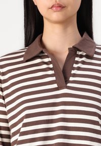 Brown and cream striped polo shirt with a soft fabric, featuring a collar and a quarter placket. Horizontal stripes run across the shirt.