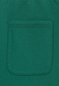 Poche en tissu vert de forme carrée avec des coutures visibles, cousue sur un fond textile vert assorti.