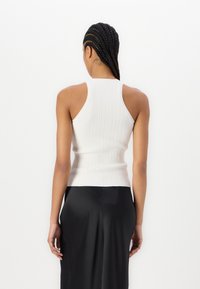 Top bianco a coste con una silhouette aderente e design a garibaldina. Texture liscia, motivo semplice e taglio a metà vita.