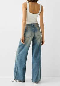 Lacláče světle modré barvy s vybledlým omběrem, obsahující zadní kapsy a vysoký pas. V kombinaci s bílým přiléhavým tílkem.