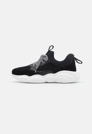 Baskets homme noir et blanc avec tige en mesh, semelle blanche épaisse, cheville rembourrée, lacets rayés et languettes au talon et à la languette.