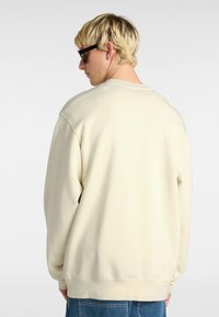 Sudadera de color beige claro con un corte relajado, cuello redondo y puños de canalé. Textura suave, diseño minimalista y sin patrones visibles.