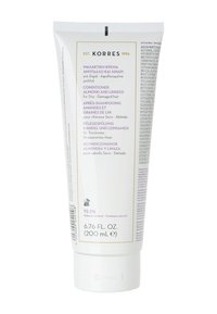 Après-shampoing en tube blanc avec un capuchon à rabat. Présente des accents violets et dorés. Le texte indique qu'il contient de l'amande et des graines de lin pour les cheveux secs et abîmés.