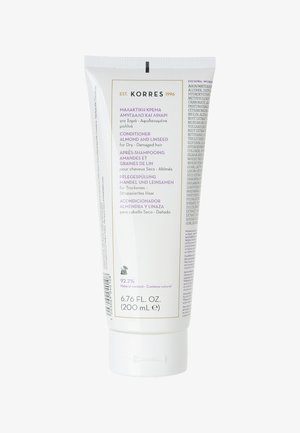 Après-shampoing en tube blanc avec un capuchon à rabat. Présente des accents violets et dorés. Le texte indique qu'il contient de l'amande et des graines de lin pour les cheveux secs et abîmés.