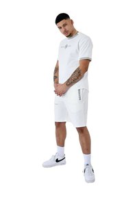 Camiseta blanca de cuello redondo con logo, pantalones cortos a juego con bolsillo lateral, combinados con zapatillas blancas y calcetines tobilleros, con detalles en negro.