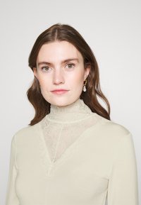 Ecrufärgad topp med hög hals och intrikata spetsdetaljer vid kragen, med en jämn textur och en slim fit-design.