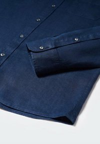 Chemise boutonnée bleu marine en tissu léger, dotée d'une poche poitrine et de boutons en argent sur les poignets et la patte de boutonnage.