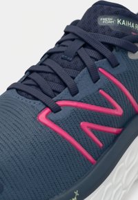 Schoenen met een marineblauwe mesh bovenwerk, roze accenten en een gestructureerd oppervlak. Heeft platte veters en een witte zool met merkaanduidingen.