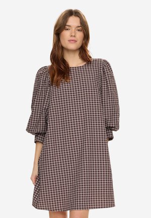 Frau mit braunen Haaren, die ein lockeres, knieumspielendes Kleid mit lila-weißem Karomuster und gepufften Dreiviertelärmeln trägt.