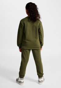 Olivgrüner Pullover und passende Jogginghose aus weichem Material mit gerippten Bündchen und lässiger Passform. Weiße und graue Turnschuhe.