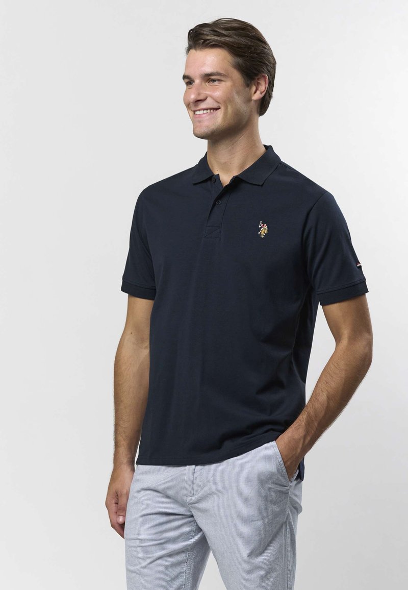 Polo bleu marine en coton avec une patte de boutonnage à deux boutons et un petit logo brodé sur la poitrine. Manches courtes et coupe ajustée.