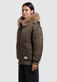Brown puffer jacket with a fur-lined hood, multiple pockets, zippers, and ribbed cuffs. Smooth texture and boxy silhouette.