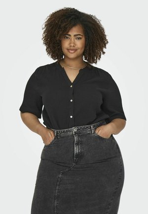 Schwarzes kurzärmliges Hemd mit Knopfverschluss und V-Ausschnitt. Aus strukturiertem Stoff. Kombiniert mit einem high-waisted dunklen Jeansrock.