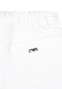 Indumento in tessuto bianco con cintura elastica e un logo argentato "EVA" su una tasca posteriore. Presenta cuciture visibili e un design della tasca testurizzato.