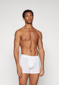 Fehér pamut boxer alsónadrág puha derékkal, testhez álló fazonban, combközép hosszúságban, egy izmos alkatú modellen bemutatva.
