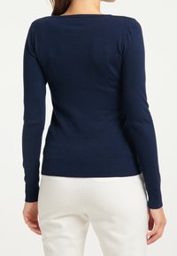 Mörkblå långärmad stickad topp med rund halsringning samt ribbat fåll och ärmslut, med en figurnära silhuett och slät textur.