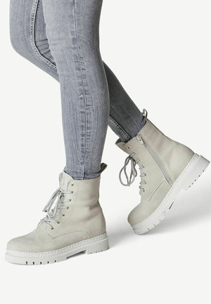 Botas de combate de cuero gris claro con un acabado texturizado, cordones y una cremallera lateral, combinadas con jeans ajustados grises. Suela de goma con agarre.