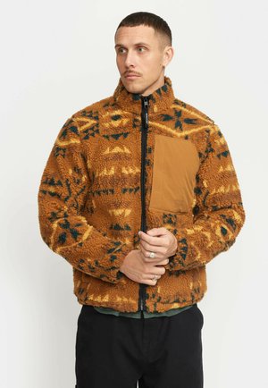 Brown textured fleece jacket with geometric patterns in yellow and dark green. Features a zip closure and a chest pocket in tan fabric.