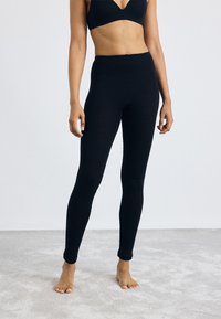 Black leggings made of a soft, stretchy fabric. High-waisted design, fitted shape, with a smooth texture and ankle-length cut.