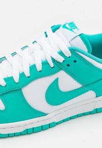 Baskets Nike blanches et turquoise avec lacets blancs, logo swoosh turquoise et détail de semelle turquoise sur fond blanc.