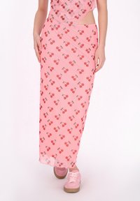 Roze maxi-rok met kersenpatroon, van lichte stof, rechte snit en een lichte glans; gecombineerd met roze sneakers met veters.