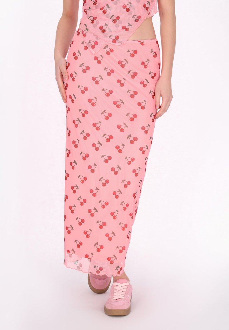 Roze maxi-rok met kersenpatroon, van lichte stof, rechte snit en een lichte glans; gecombineerd met roze sneakers met veters.