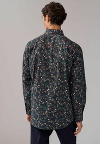 Langärmliges Shirt aus dunkelgrünem Stoff mit floralem Muster in Pink und Weiß. Klassischer Kragen und abgerundeter Saum.