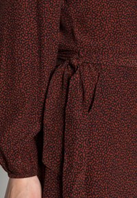 Tessuto per un vestito con motivo rosso e nero, dotato di un dettaglio in vita legato. La texture appare leggera, con maniche lunghe e gather.