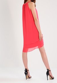Rosa ärmelloses Kleid mit einem lagenförmigen Saum, aus leichtem Stoff gefertigt. Es hat einen Schlüsselaugen-Ausschnitt im Rücken und wird mit schwarzen High-Heels kombiniert.
