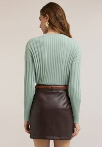 Mátově zelený žebrovaný svetr s dlouhými rukávy v kombinaci s hnědou koženou mini sukní a hnědým páskem, pohled zezadu.