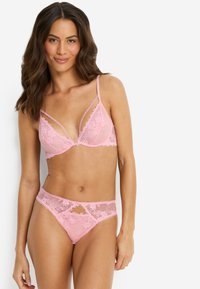 Rosa blonde-BH med dyp utringning og dekorativ kant, kombinert med matchende blonde-tanga med utskjæring og blomsterdekor.