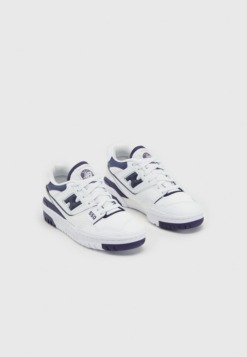Baskets New Balance 550 blanches et bleu marine avec lacets, logo sur le côté et détails perforés sur un fond clair uni.