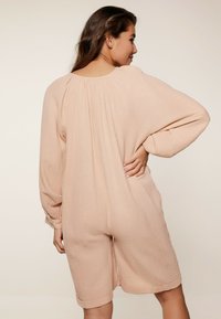 Romper rosa blush realizzato in tessuto testurizzato, con maniche lunghe, vestibilità morbida e tasche laterali, con dettagli arricciati sullo scollo.