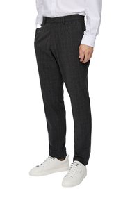 Pantalons à carreaux gris en tissu à texture lisse. Design ajusté avec poches latérales, associés à des baskets blanches.