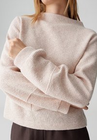Maglione rosa chiaro lavorato a maglia con un motivo testurizzato, design corto e maniche larghe. Il tessuto sembra morbido e accogliente.