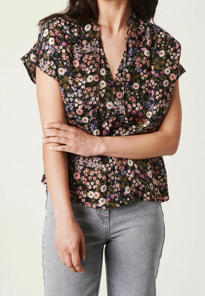 Zwarte bloemenblouse met korte mouwen, versierd met roze, witte en paarse bloemen op een donkere achtergrond. Lichtgewicht stof, ontspannen pasvorm.