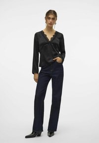 Sort satin langærmet top med blondekanter ved v-udskæringen, parret med mørk denim flared bukser, båret med sorte spidse ankelstøvler.