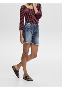 Gestreiftes Langarmshirt in Rot und Marineblau, kombiniert mit verwaschenen Jeansshorts mit ausgefransten Säumen. Als Schuhwerk dienen schwarze Riemchensandalen mit doppelten Schnallen.