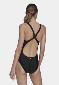 Black one-piece swimsuit featuring a cross-back design, cut-out back, and smooth texture. Minimalist branding on the lower back.
