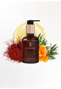 Bouteille en verre brun avec un distributeur à pompe, étiquetée "True Botanicals Phyto-Retinol Lotion Corporelle Anti-Âge", entourée de baies oranges et de poudre rouge.