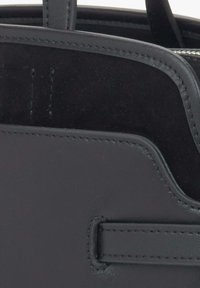 Czarna skórzana torebka o teksturowym wykończeniu, z subtelnymi przeszyciami, gładką górną krawędzią oraz częściowo widoczną podszewką.