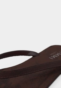 Καφέ δερμάτινο σανδάλι μεσαίας φάσης με λεπτές λουριά και επίπεδη σόλα, φωτογραφημένο σε απλό φωτεινό φόντο.