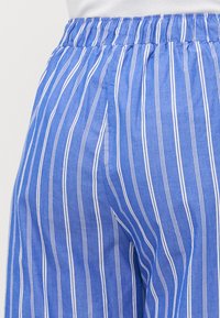 Blue and white striped pants with a relaxed fit and elastic waistband. Material appears lightweight and textured with vertical lines.