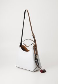 Sac à main en cuir blanc de forme triangulaire, avec une bandoulière ajustable marron et noire, et un accent en forme de pampille décorative en bordeaux et marron.